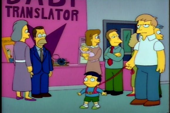 A distressed-looking toddler is in a harness and leash, held by his father, in front of a "baby translator" booth.